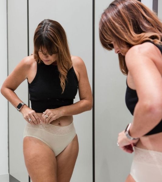 Woman adjusting her Sahara Period Lace Beige Panties in front of a mirror.