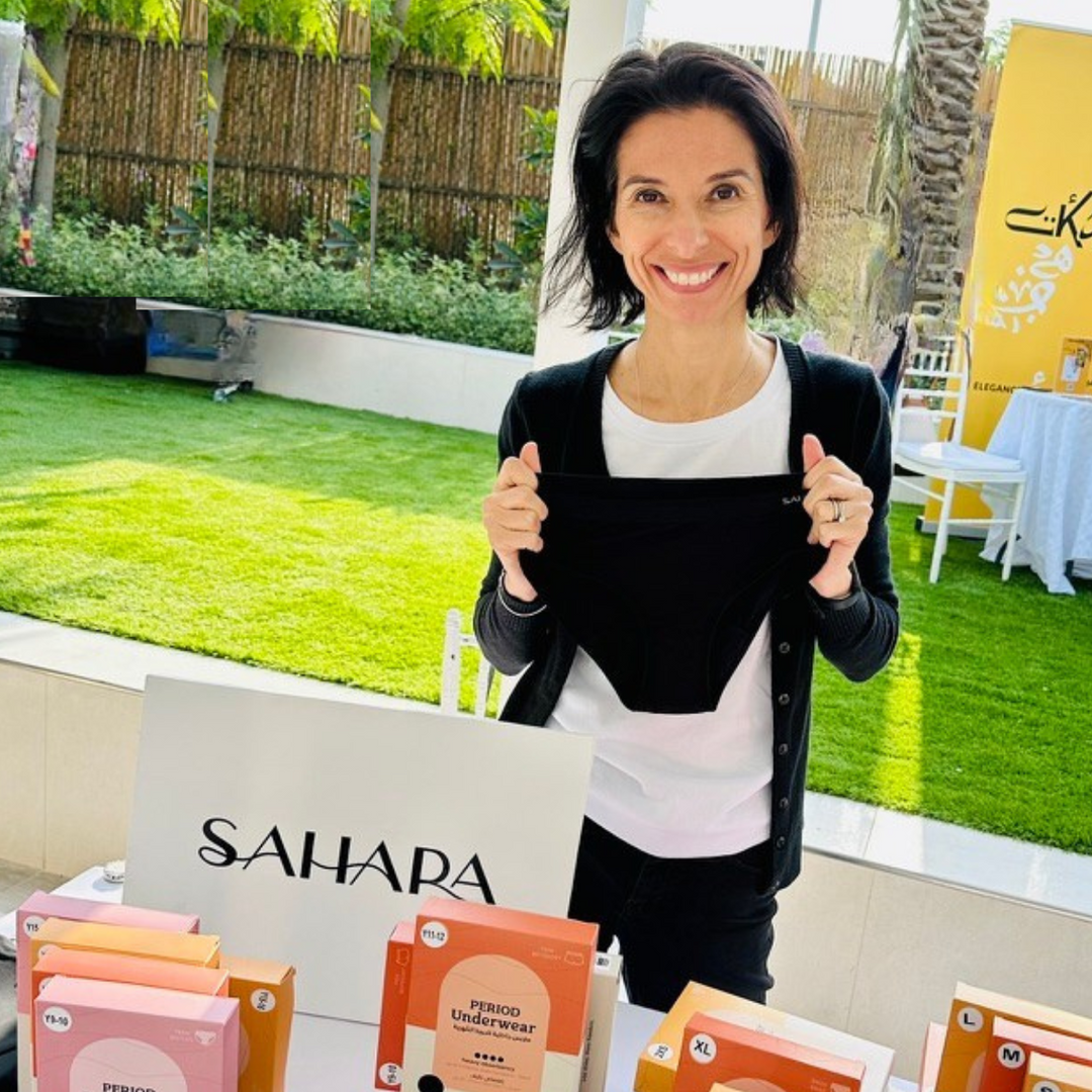 Woman holding Sahara black period pants behind Sahara branding at event.