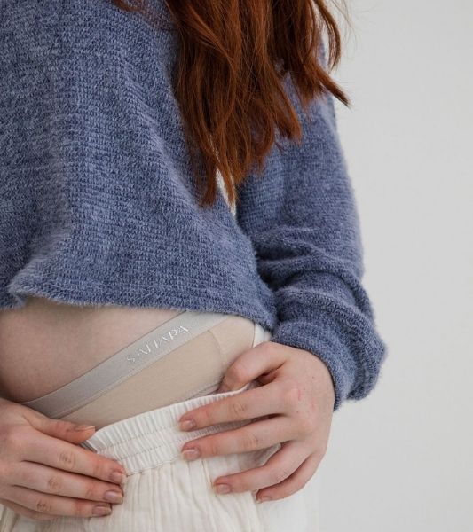 Woman wearing a blue sweater and Sahara beige period pants under white pants