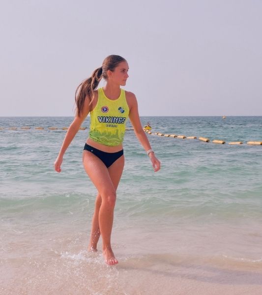 Woman in a yellow vikings top and black Sahara period swimwear walking on a beach in Dubai