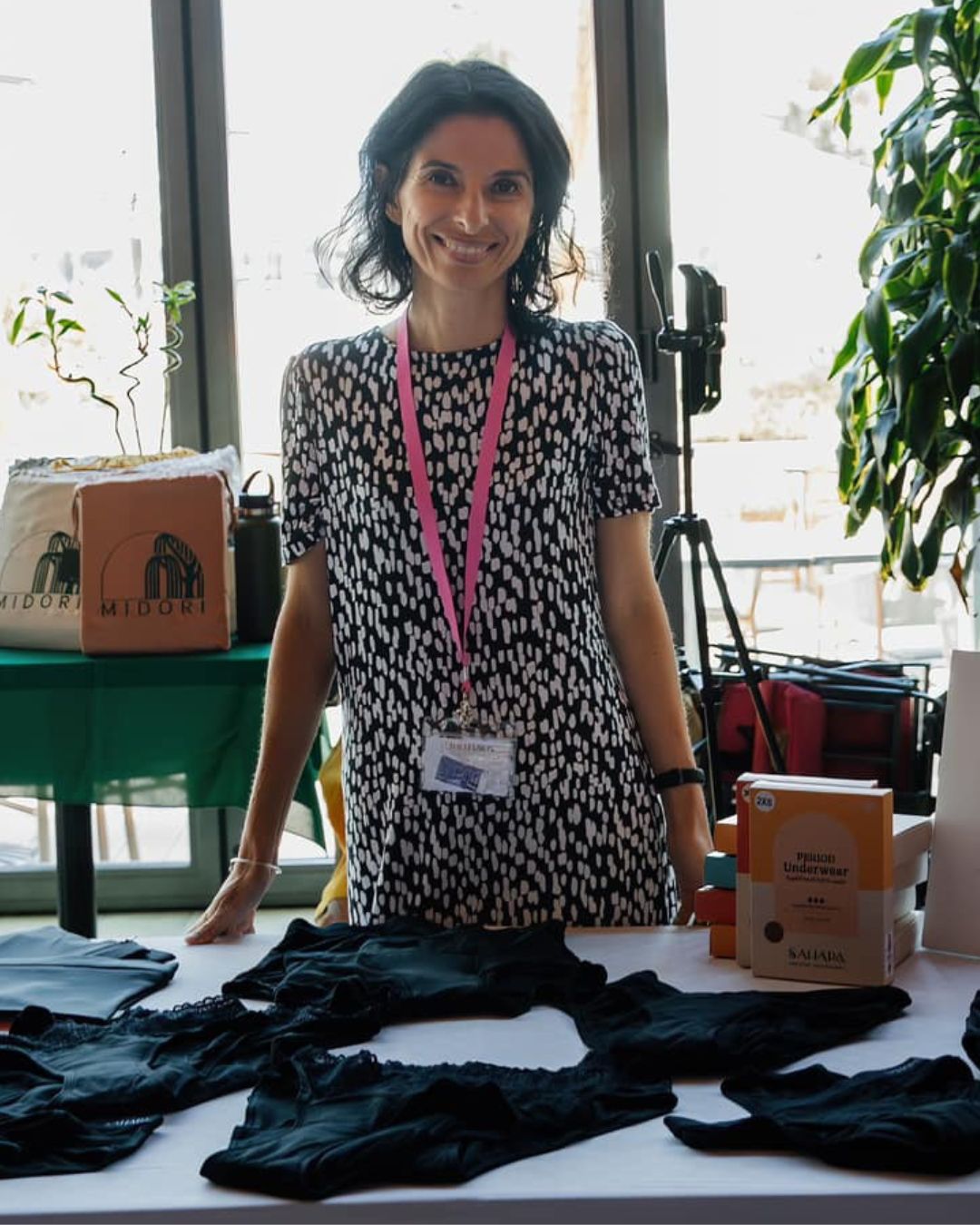 Woman standing behind a table at an event with Sahara period underwear, wearing a dress.